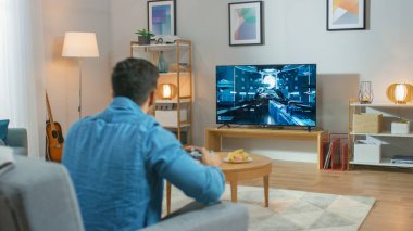 Oturma Odasında Oturan Koltuk Tutucu Denetleyicisinde Bir Konsol Video Oyunu 'nda Oynayan 3d Eylem Atıcısı Oyunu TV' de gösterildi.