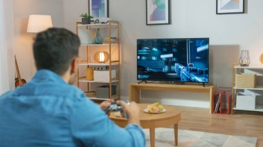 Oturma Odasında Oturan Koltuk Tutucu Denetleyicisinde Bir Konsol Video Oyunu 'nda Oynayan 3d Eylem Atıcısı Oyunu TV' de gösterildi.