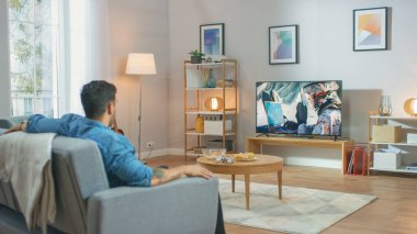 Oturma odasında, Adam TV 'de bir koltukta oturup savaş filmi seyrediyor. Savaş Askeriyle Çağdaş Savaş Hareketi Televizyonda Gösterildi.
