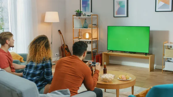 En la sala de estar Tres amigos juegan videojuegos en la pantalla clave de croma verde, utilizando controladores. Adolescentes divirtiéndose en casa . —  Fotos de Stock