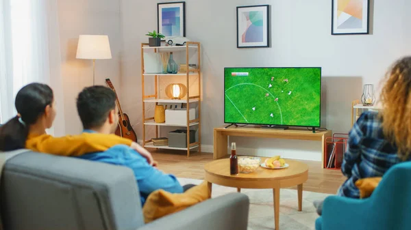 En casa Diverse Grupo de Deportes Fans Relojes partido de fútbol importante en la televisión, Ellos animan al equipo. Acogedora habitación con aperitivos y bebidas sobre la mesa . —  Fotos de Stock