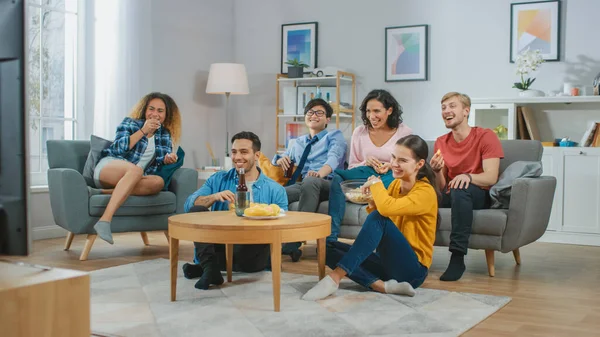 Zu Hause sitzen diverse Gruppenfreunde zusammen vor dem Fernseher, essen Snacks und trinken Getränke. Sitcom oder Film gucken, gemeinsam lachen und Spaß haben. — Stockfoto