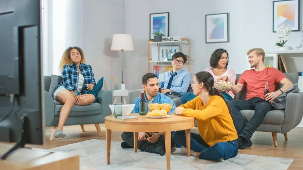 Zu Hause sitzen diverse Gruppenfreunde zusammen vor dem Fernseher, essen Snacks und trinken Getränke. Sitcom oder Film gucken, gemeinsam lachen und Spaß haben. — Stockfoto