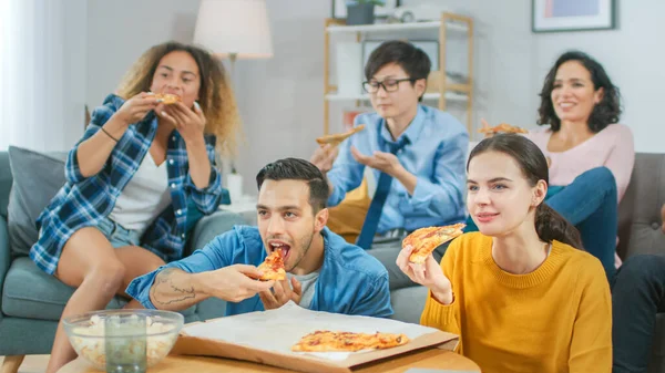 En casa Diverse Group Amigos viendo la televisión juntos, comparten pizza gigantesca, comiendo sabrosas piezas de pastel. Chicos y chicas viendo comedia Sitcom o una película, riéndose y divirtiéndose juntos . — Foto de Stock