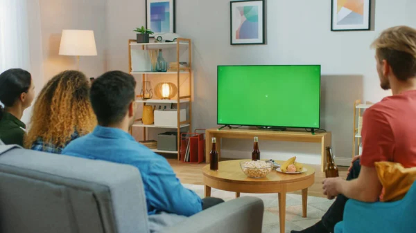 Amigos felices sentados en casa viendo la pantalla clave de croma verde, relajándose en un sofá. Ver partidos deportivos, Noticias, Sitcom TV Show o una película . —  Fotos de Stock