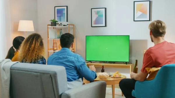 Amigos felices sentados en casa viendo la pantalla clave de croma verde, relajándose en un sofá. Ver partidos deportivos, Noticias, Sitcom TV Show o una película . —  Fotos de Stock