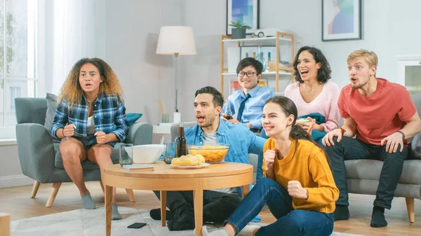 In de woonkamer Diverse groep vrienden op kijken naar sport Game Match op TV, Ze Cheer en Chant voor het team, Vieren overwinning na Team Scoring Winning Goal. Gezellige kamer met snacks en drankjes — Stockfoto