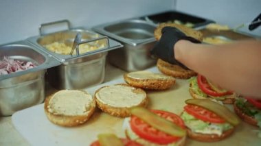Hamburger Hazırlayan Aşçının Lezzetli Yakın Çekimi. Yemek Şefi, Susam Tohumu ile Çörekler 'in üstüne Souce ekliyor. Biftekli Taze Gurme Burgerler, Salata, Domates ve Salatalık Hazırlanıyor.