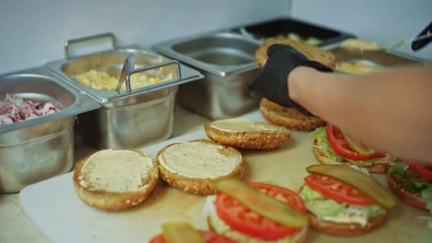 Leckere Nahaufnahmen eines Kochs beim Zubereiten von Burgern. Küchenchef gibt Soße auf Semmeln mit Sesam. Frische Gourmet-Burger mit Rinderpatty, Salat, Tomaten und Gurken werden zubereitet. — Stockvideo