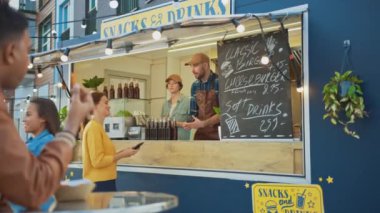 Yemek kamyonu çalışanı genç ve mutlu bir bayana taze yapılmış bir hamburger verdi. Genç bayan yiyecek parasını ödemek için NFC mobil ödemesini kullanıyor. Modern Hip Mahallesi 'nde Sokak Yemekleri Satıyor.
