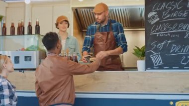 Yemek kamyonu çalışanı Deri Ceketli Genç Bir Adama Limonata ve Burger Veriyor. Hintli Adam yemek parasını ödemek için Kontaksız Banka Kredi Kartı kullanıyor. Sokak Yemekleri Kamyonu Açık havada Burger Satıyor.