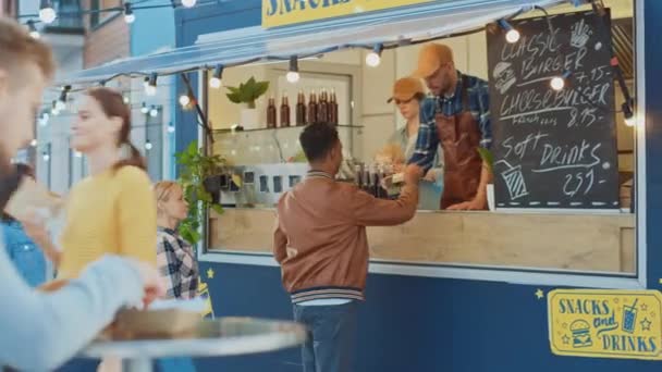 Un employé de Food Truck distribue un hamburger à un jeune homme heureux en veste en cuir. Indian Man utilise la carte de débit bancaire sans contact pour payer la nourriture. Camion alimentaire de rue Vendre des Burgers en plein air . — Video