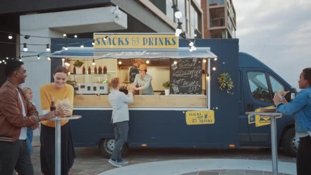 Pracownik ciężarówki z jedzeniem rozdaje świeżo wykonane hamburgery dla szczęśliwego młodego człowieka w garniturze. Kobieta uśmiecha się i patrzy w kamerę. Street Food Truck Sprzedawanie hamburgerów w nowoczesnej dzielnicy. — Wideo stockowe