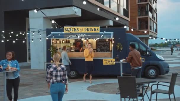 Un employé de Food Truck distribue des hamburgers de boeuf fraîchement préparés, des frites et des boissons froides aux jeunes clients heureux de Hipster. Camion commercial vendant de la nourriture de rue dans un quartier frais moderne. — Video