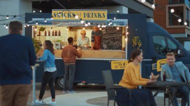 Yemek kamyonu çalışanı Mutlu Genç Hipster Müşterilerine Yeni Yapılmış Biftek Burgerleri, Kızartmalar ve Soğuk İçecekler Veriyor. Modern Havalı Mahallede Sokak Yemeği Satan Ticari Kamyon.