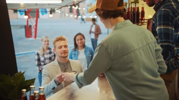 Jídlo Truck Zaměstnanec Ruce ven čerstvě vyrobené Burger na šťastný mladý muž v obleku. Muž platí za potraviny s bezkontaktní kreditní kartou. Street Food Truck Prodej hamburgery v moderní čtvrti Hip — Stock video