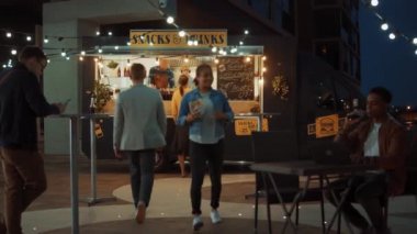 Yemek kamyonu çalışanı Mutlu Genç Hipster Müşterilerine Yeni Yapılmış Biftek Burgerleri, Kızartmalar ve Soğuk İçecekler Veriyor. Modern Havalı Mahallede Sokak Yemeği Satan Ticari Kamyon.