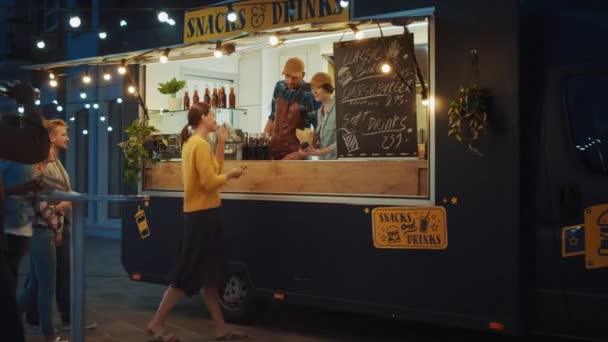 Un employé de Food Truck distribue des hamburgers de boeuf fraîchement préparés, des frites et des boissons froides aux jeunes clients heureux de Hipster. Camion commercial vendant de la nourriture de rue dans un quartier frais moderne. — Video
