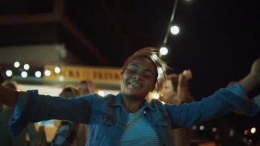 Bir grup arkadaş, Sokak Yemekleri Kafesi 'nin dışında parti veriyor. Müzik eşliğinde dans eden güzel bir kadının portresi. Modern Mahallede Akşam Vakti. Herkes mutlu ve neşeli.