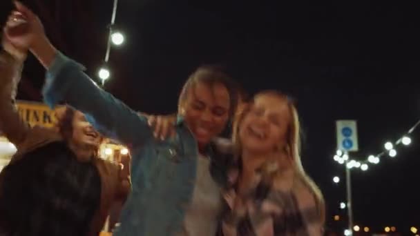 Vriendengroep geeft een feestje buiten een Street Food Burger Cafe. Twee mooie meisjes knuffelen en dansen op muziek. Het is avond in een moderne buurt. Iedereen is gelukkig en vol vreugde.. — Stockvideo