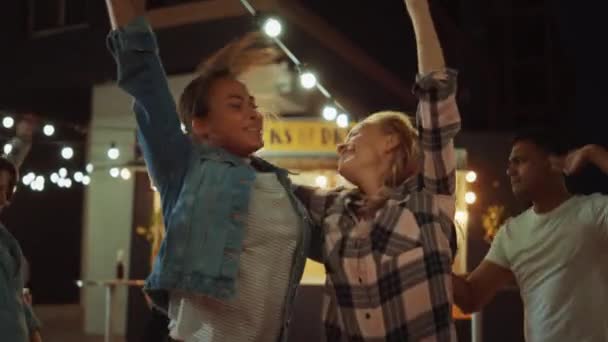 Grupp av vänner har fest utanför en Street Food Burger Cafe. Två vackra flickor som kramas och dansar till musik. Det är kväll i ett modernt grannskap. Alla är glada och fulla av glädje. — Stockvideo