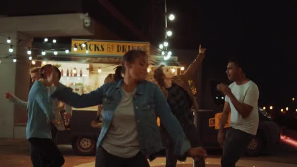 Група друзів влаштовує вечірку за межами кафе для бургерів вуличної їжі. Портрет молодої красивої жінки, що танцює на музику. Вечір у сучасному сусідстві. Усі щасливі і щасливі — стокове відео