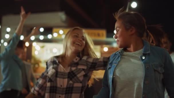 Grupo de amigos están teniendo una fiesta fuera de un Street Food Burger Café. Two Beautiful Girls Hugging and Dancing to Music (en inglés). Es de noche en un barrio moderno. Todos son felices y llenos de alegría . — Vídeo de stock