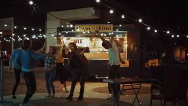 Groupe d'amis font une fête en dehors d'un café Burger Street Food. Ils dansent et passent à la musique tendance. C'est le soir dans un quartier moderne et cool. Tout le monde est heureux et plein de joie . — Video