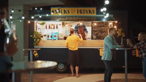 Food Truck Medewerker reikt een vers gemaakte hamburger uit aan een vrolijke jonge vrouw. Jongedame betaalt voor eten met contactloze creditcard. Street Food Truck verkoopt hamburgers in een moderne hippe buurt — Stockvideo