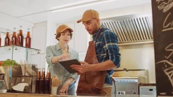 Sucesso Food Truck Man e Mulher Funcionários em Brown Caps estão usando um computador tablet. Eles discutem seus lucros e planos de negócios futuros. Caminhão comercial ou quiosque que vende comida de rua e bebidas . — Vídeo de Stock