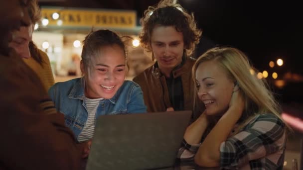 Hermosos y guapos amigos están usando una computadora portátil mientras están de pie en una mesa en un café de comida de la calle al aire libre. Están viendo un video o una transmisión en línea. Son felices y sonríen . — Vídeos de Stock