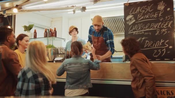 Jedzenie Truck Pracownik Ręce obecnie świeżo wykonane hamburgera do szczęśliwej młodej kobiety. Młoda dama płaci za jedzenie kartą kredytową bez kontaktu. Street Food Truck Sprzedawanie hamburgerów w nowoczesnej dzielnicy Hip — Wideo stockowe