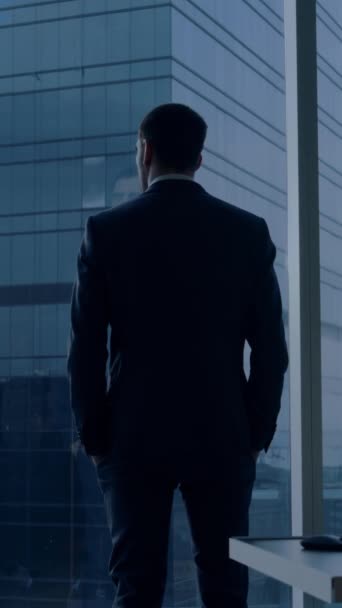 Back View of the Thoughtful Businessman wearing a Suit Standing in His Office, Contemplating Next Big Business Deal, Looking out of the Window. Video Footage with Vertical Screen Orientation 9:16 — Stock Video