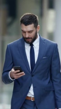 Başarılı İşadamı, Büyük Şehir İş Dünyası Caddesinde yürürken akıllı telefon kullanır. Dikey Ekran Yönelimli Video Görüntüsü 9: 16