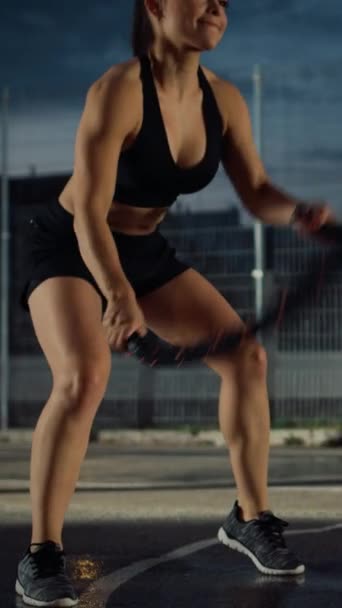 아름다운 체력의 소녀가 전투용 밧줄로 운동을 하고 있습니다. 그녀는 야외 농구 코트에서 연습하고 있습니다. 수직 화면 방향의 비디오 영상 — 비디오
