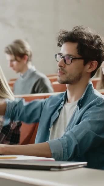 Gutaussehender hispanischer Student nutzt Laptop-Hörvorlesung an der Universität, hebt die Hand und stellt Dozent eine Frage. multiethnische Gruppe von Studenten. Videomaterial mit vertikaler Bildschirmausrichtung 9: 16 — Stockvideo