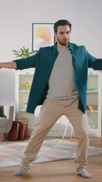 Ein fröhlicher junger Mann tanzt mitten im Wohnzimmer. Lustiger Mann tanzt kreativ und professionell zu Hause. Videomaterial mit vertikaler Bildschirmorientierung — Stockvideo