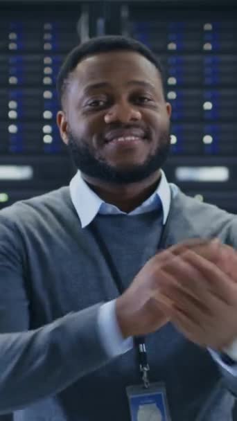Бородатый черный ИТ-инженер стоит и позирует со скрещенными руками в центре обработки данных серверной комнаты с серверными компьютерами, работающими на стойке. Видео с вертикальным экраном Ориентация 9: 16 — стоковое видео