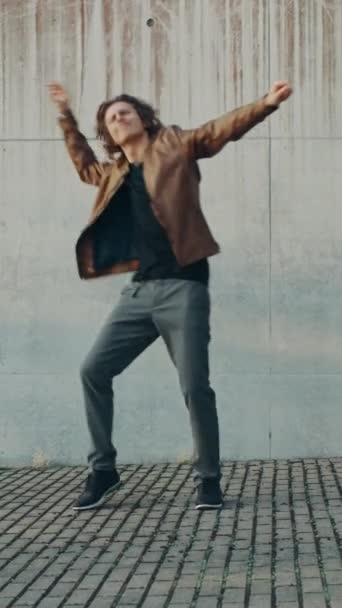 Cheerful and Happy Young Man with Long Hair Actively Dancing While Walking Down the Stairs. He's Wearing a Brown Leather Jacket. Vertical Screen Orientation Video 9:16 — Stock Video