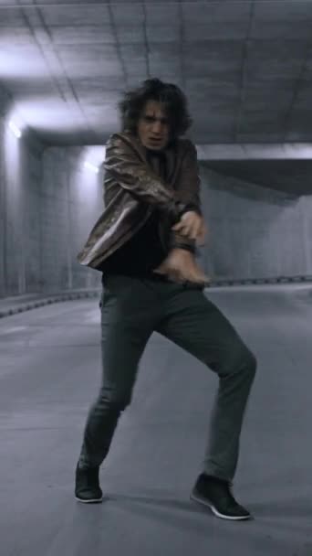긴 머리를 가진 진지하고 쿨 한 젊은 힙합 선수가 커다란 콘크리트 벽 옆의 거리에서 열정적으로 춤을 추고 있습니다. 수직 화면 방향 비디오 9: 16 — 비디오