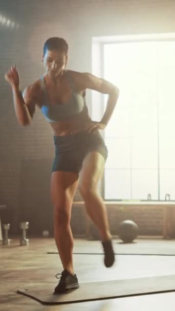 Strong and Fit Beautiful Athletic Woman in Sport Top and Shorts está haciendo ejercicios de marzo de pie en un gimnasio industrial de estilo loft con carteles motivacionales. Vídeo de orientación vertical de la pantalla 9: 16 — Vídeos de Stock