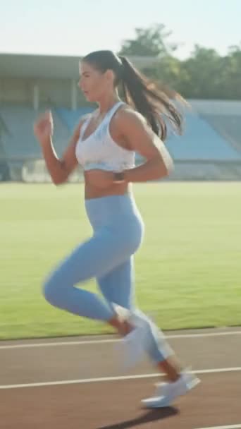 Belle femme de remise en forme en haut et leggings athlétiques bleu clair commence une course de sprint dans un stade extérieur. Au ralenti. Orientation verticale de l'écran Vidéo 9 : 16 — Video