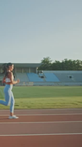 Hermosa mujer de fitness en azul claro Athletic Top y Leggings está comenzando una carrera de sprint en un estadio al aire libre. Atleta haciendo su práctica deportiva. A cámara lenta. Vídeo de orientación vertical de la pantalla 9: 16 — Vídeos de Stock