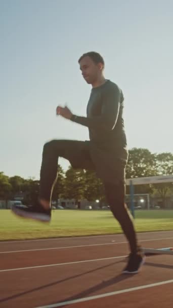 Athletic Fit Man i grå tröja och shorts Hurdling i stadion. Han hoppar över barriärer på en varm sommareftermiddag. Slow Motion Tracking Skott. Vertikal skärmorientering Video 9: 16 — Stockvideo