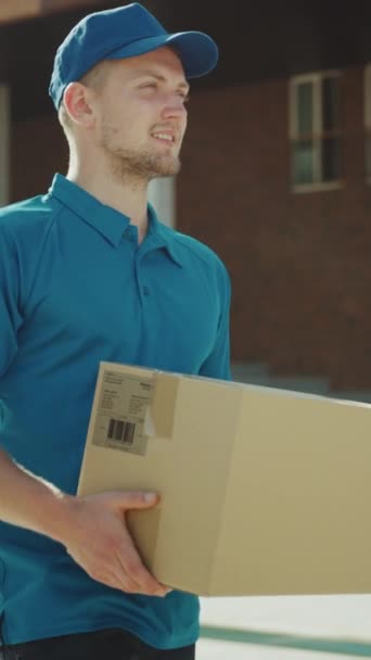 Handsome Delivery Man Holds Cardboard Box Package Berjalan Melalui Modern Stylish Business District. Gerakan Lambat Sudut Rendah. Orientasi Layar Vertikal Video 9: 16 — Stok Video