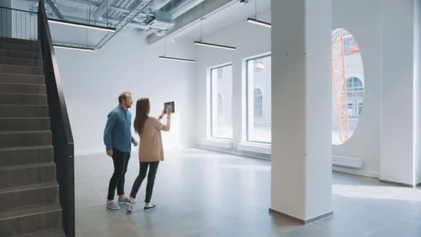 年轻的嬉皮士男人和女人站在一个空荡荡的白色办公室里，用一个放大的现实软件在桌面上描绘它。 阳光透过大窗户照耀。 房间设有录象软件追踪点. — 图库视频影像