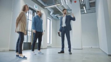 Genç Erkek ve Bayan Hippilere Yeni Boş Ofis Alanını Gösteren Emlakçı. Girişimciler Komisyoncuyla bir tabletle buluştu ve satın almak veya kiralamak istedikleri tesisi tartıştılar.