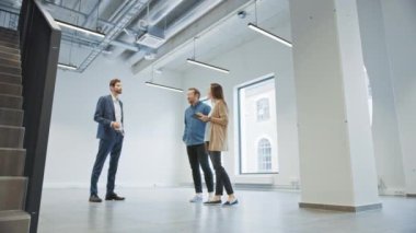 Genç Erkek ve Bayan Hippilere Yeni Boş Ofis Alanını Gösteren Emlakçı. Girişimciler Komisyoncuyla bir tabletle buluştu ve satın almak veya kiralamak istedikleri tesisi tartıştılar.