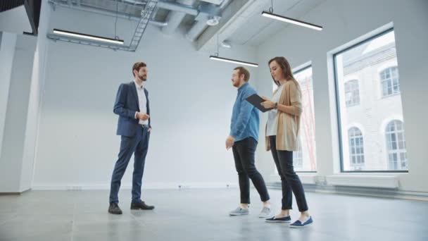 Agent immobilier montrant un nouvel espace de bureau vide aux jeunes hipsters masculins et féminins. Les entrepreneurs rencontrent le courtier avec une tablette et discutent de la facilité qu'ils souhaitent acheter ou louer. — Video