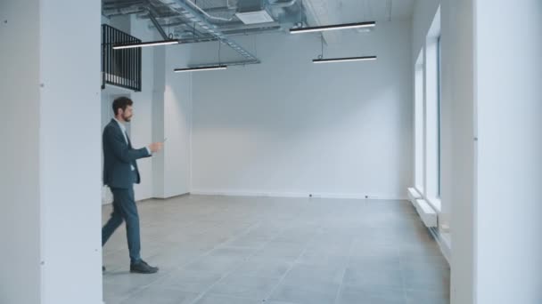 Biznesmen stojący w pustym biurze i mapujący go za pomocą rozszerzonego oprogramowania rzeczywistości na tablecie. Przedsiębiorca nosi kombinezon. Pokój posiada punkty śledzenia dla oprogramowania wideo. — Wideo stockowe